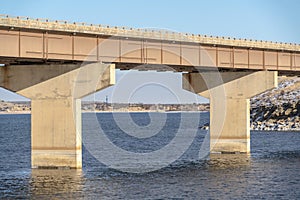 Focus on a beam bridge supported by abutments over blue lake against cloudy sky