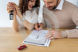 Focus of bearded man signing contract near woman holding car key