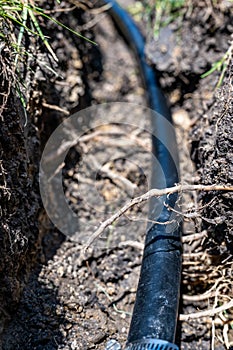 Focus on a black 1 inch sprinkler plastic water line laid in a shallow trench