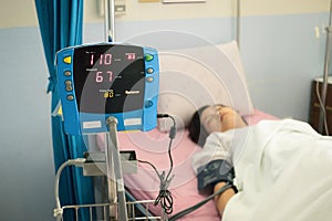 Focus on blood pressure monitor with patient on bed in hospital ward. Medical concept