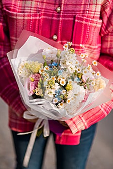 Focus on bouquet of various colorful flowers and field daisies in white matte wrapping paper