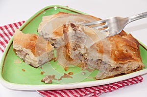 Focus on a burek on the fork with burek in the background