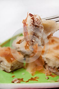 Focus on a burek on the fork with burek in the background