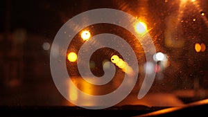 Focus on the car`s windshield. Rain drips on it. The wipers are working. The night street is lit by streetlights and a blinking tr