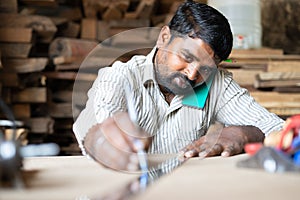 Focus on carpainter, young carpainter busy taking orders from customer on mobile phone while working at carpentry shop -