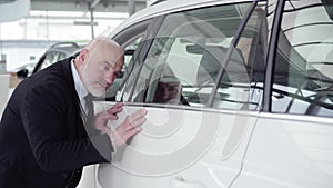 Focus changes from face of satisfied client to hand of man touching new white car in dealership. Confident successful