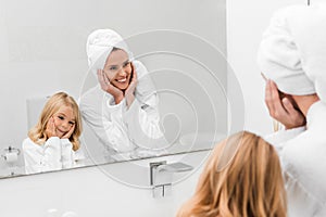 Focus of cheerful mother and cute daughter in bathrobes touching faces in bathroom