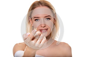 Focus on contact lens on finger of young woman. Young woman holding contact lens on finger in front of her face. Woman