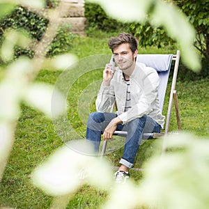 Focus on a cute young man waiting on telephone outdoors