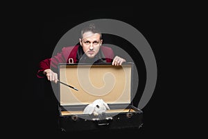 Focus disappearance white rabbit in suitcase, magician conjures magic wand, black background photo