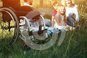 Focus on emply wheelchair on the foreground while happy family rest on the background