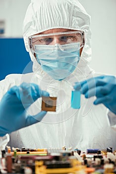 Focus of engineer holding microchip and glass container with blue liquid near computer motherboard