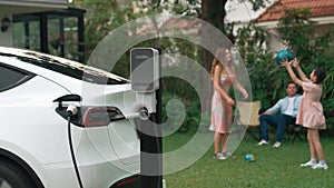 Focus EV station recharging battery for EV car on blurred family. Fastidious