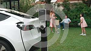 Focus EV station recharging battery for EV car on blurred family. Fastidious