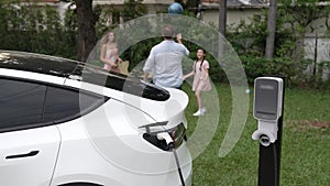 Focus EV station recharging battery for EV car on blurred family. Fastidious