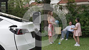 Focus EV station recharging battery for EV car on blurred family. Fastidious