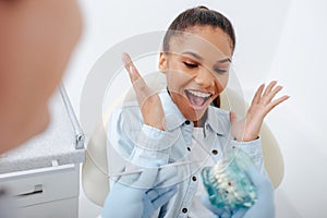 Focus of excited african american woman in braces gesturing near dentist holding teeth model