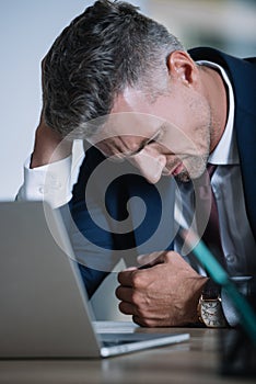 Focus of frustrated businessman in formal wear near laptop in office