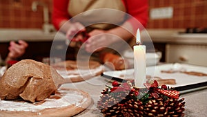 Focus on gingerbread dough and candle on candlestick against blurred mom and daughter kneading the dough. Christmas mood