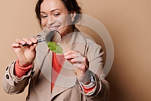 Focus on green leaf in hands of a blurred woman, attentively studying the structure of a plant through magnifying glass