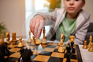 Focus on the hand of a blurred handsome boy holding a chess piece above the chessboard and making a move during the game. Smart