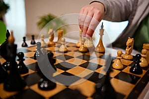 Focus on the hand of an unrecognizable child holding a chess piece above the chessboard and making a move during the game. Smart