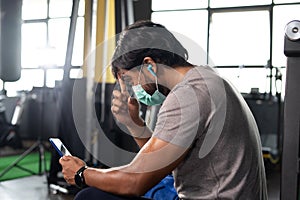 focus on hand, young indian body builder with medical face mask cleaning sweat while using mobile phone at gym - concept