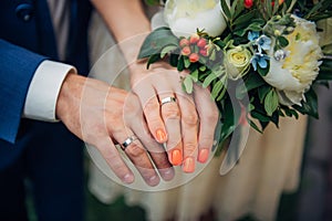 Focus on the hands of bride and groom, wedding bouquet, top view, blurred background. Platinum or silver rings on the fingers of