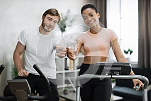 Focus on hands with water bottle of attractive female and male working out on fitness