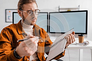 Focus of handsome digital designer holding pen and notebook in office