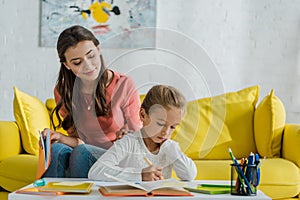 Focus of happy babysitter sitting on sofa and looking at cute kid studying at home