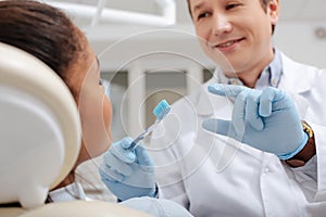 Focus of happy dentist gesturing near african american woman while holding toothbrush