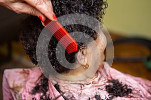 Focus on the head of a senior woman, whose hairdresser is styling her hair. They are at home and the older woman who is styling