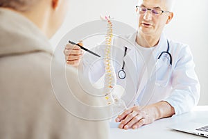 Focus on human spine model pointing by Middle aged male doctor and explaining patient his problem in medical clinic