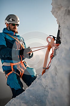 Focus on ice axe. Man climber with equipment and ropes on the slope at background