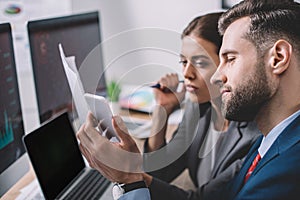 Focus of information security analysts using smartphone while working near computers in office