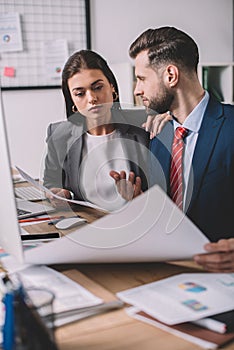 Focus of information security analysts working with papers near computers on table in office