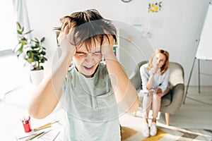 Focus of irritated kid with dyslexia shouting and holding head