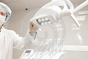 Focus on the lamp, the doctor turns lights. . Young man dentist in dental clinic. Medicine, health, stomatology concept