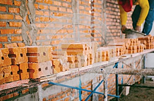 Focus on the orange bricks within the construction site where construction workers are working. The orange bricks are stacked and