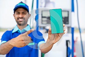 focus on phone, Smiling petrol pump worker showing green screen mobile phone by pointing finger by looking at camera at