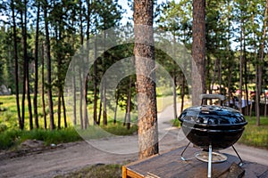 Focus on a portable charcoal grill at a campsite overlooking a green forest