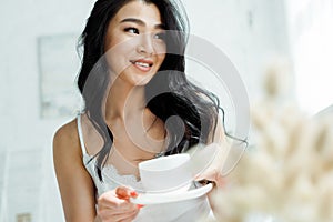 Focus of positive thai woman holding cup with tea