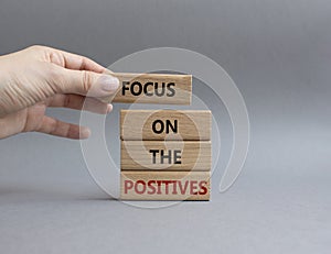 Focus on the Positives symbol. Concept word Focus on the Positives on wooden blocks. Beautiful grey background. Businessman hand.