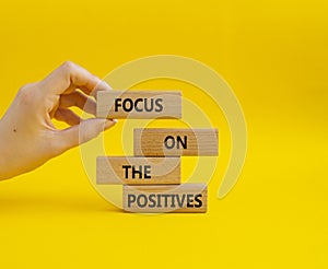 Focus on the Positives symbol. Concept word Focus on the Positives on wooden blocks. Beautiful yellow background. Businessman hand photo