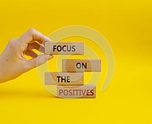 Focus on the Positives symbol. Concept word Focus on the Positives on wooden blocks. Beautiful yellow background. Businessman hand