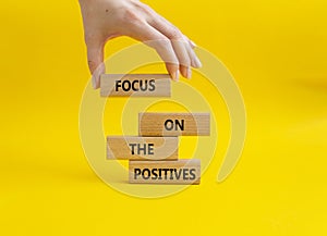 Focus on the Positives symbol. Concept word Focus on the Positives on wooden blocks. Beautiful yellow background. Businessman hand photo