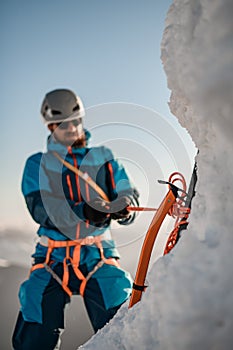 Focus on professional ice axe. Man climber with equipment and ropes on the slope at background