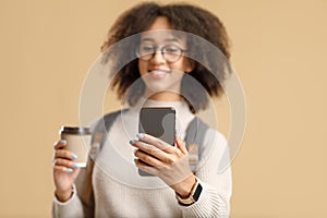 Focus on smartphone with empty space in hands of african american woman with backpack and glasses holding cup of coffee