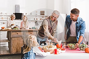 Focus of smiling father and grandparent looking at kid and setting table in Thanksgiving day